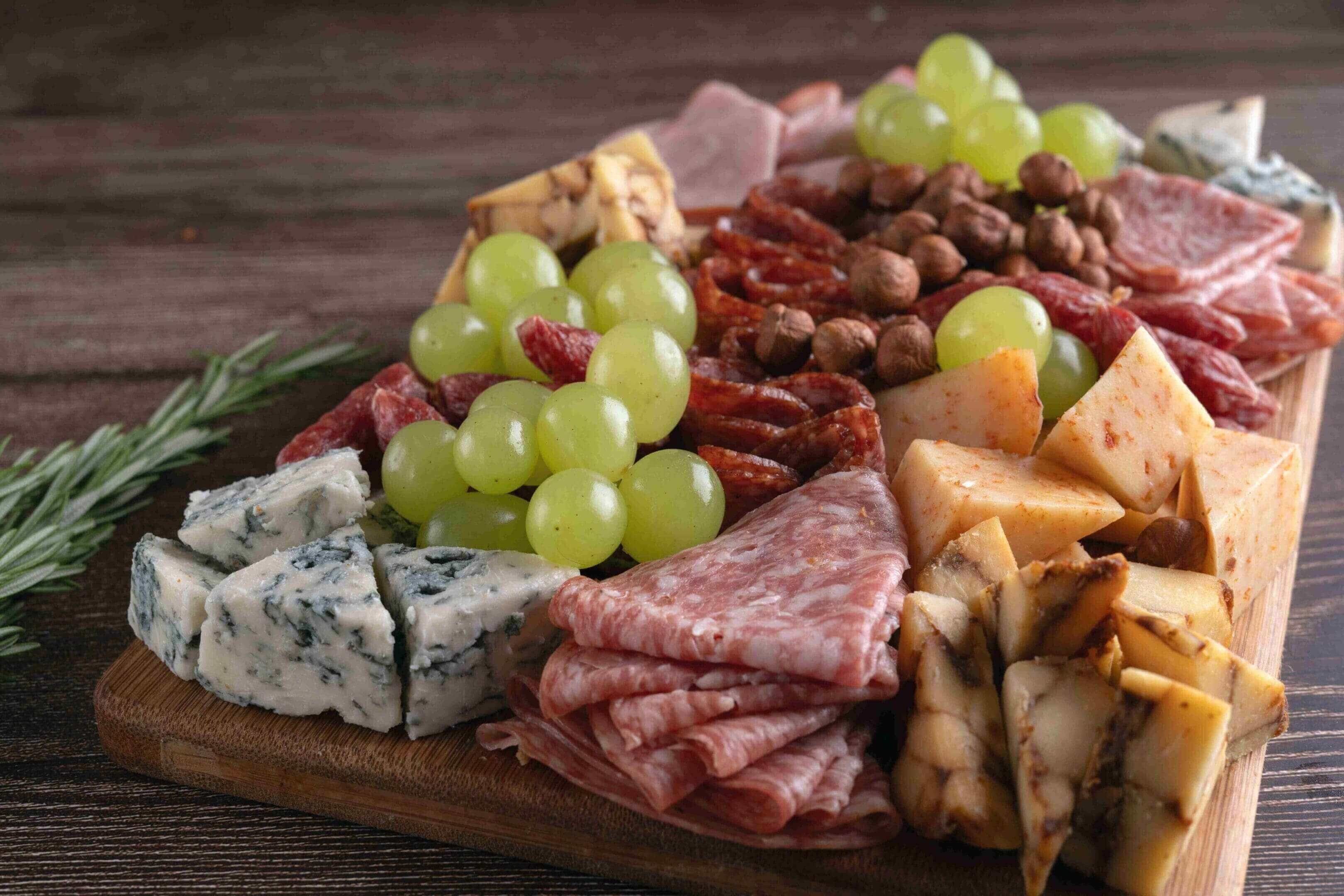 A charcuterie board with meats, cheeses, grapes, and nuts.
