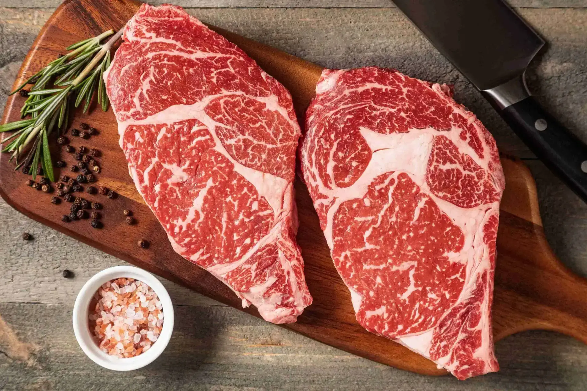 Two raw ribeye cuts beside coarse pink salt