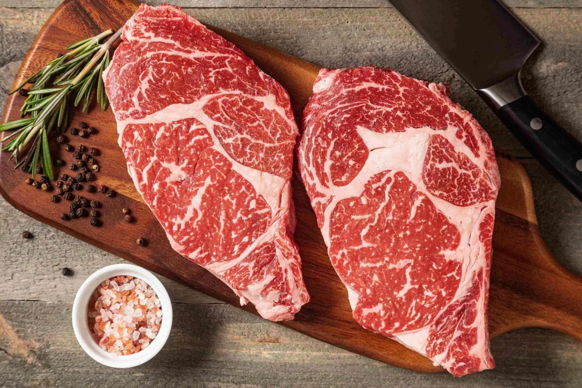 Marbled ribeye steaks on wooden board with rosemary